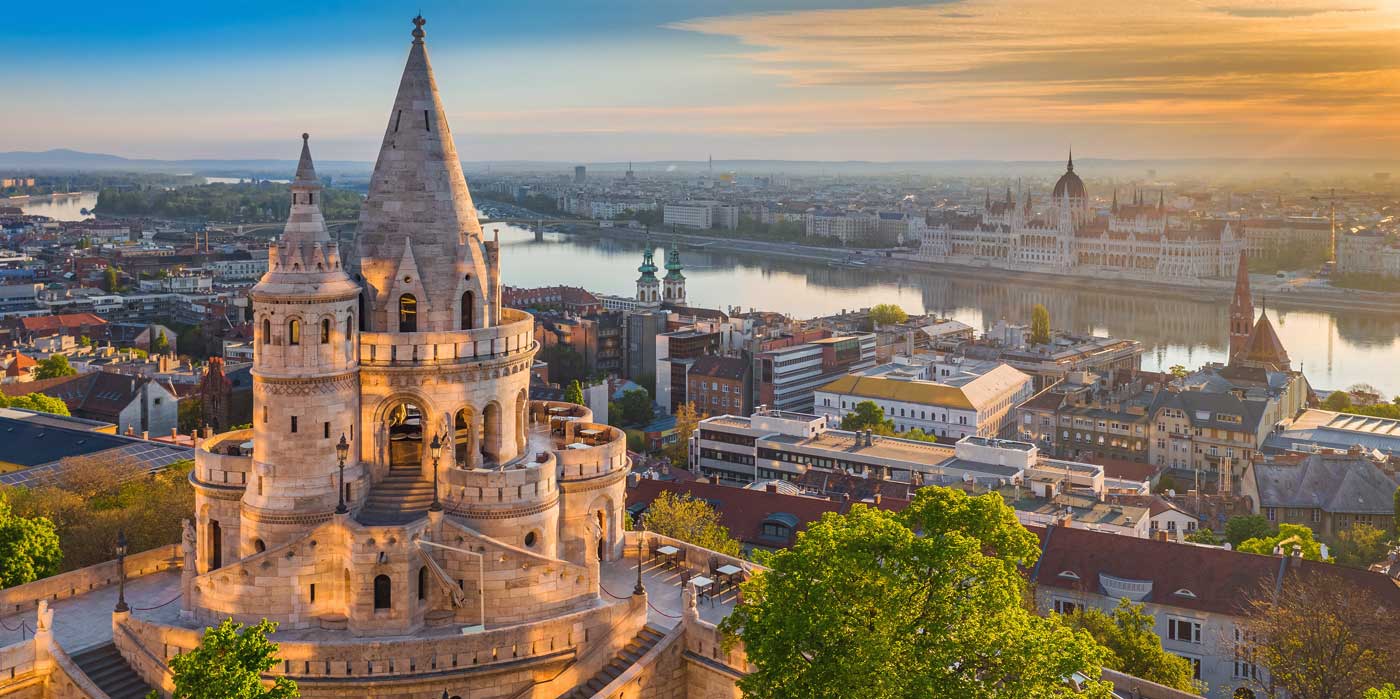 Budapest, Hungary - Beautiful golden summer sunrise with the tower of Fisherman's Bastion and green trees. Parliament of Hungary and River Danube at background. Blue sky.