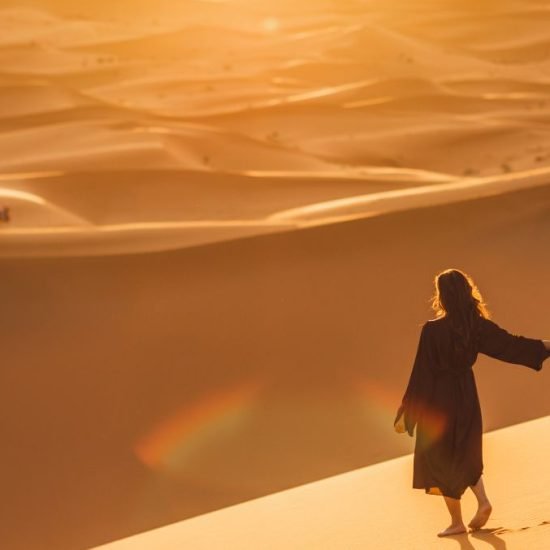 Couple walking in Sahara desert at sunset. View from behind, nature background. Travel, freedom and wanderlust concept.